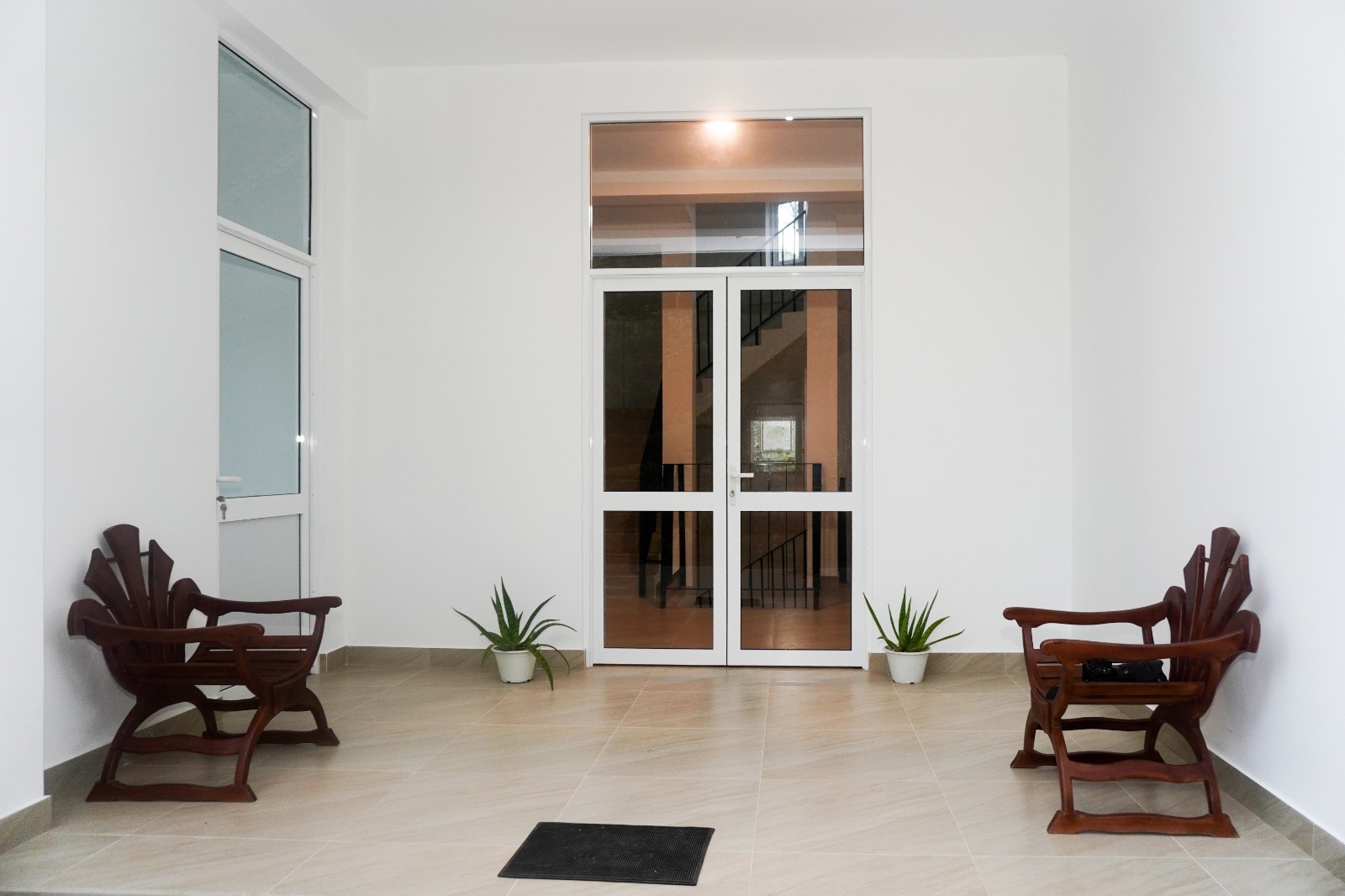 Entrance lobby at Romara Living with two carved wooden chairs, potted aloe plants and glass doors to the stairway