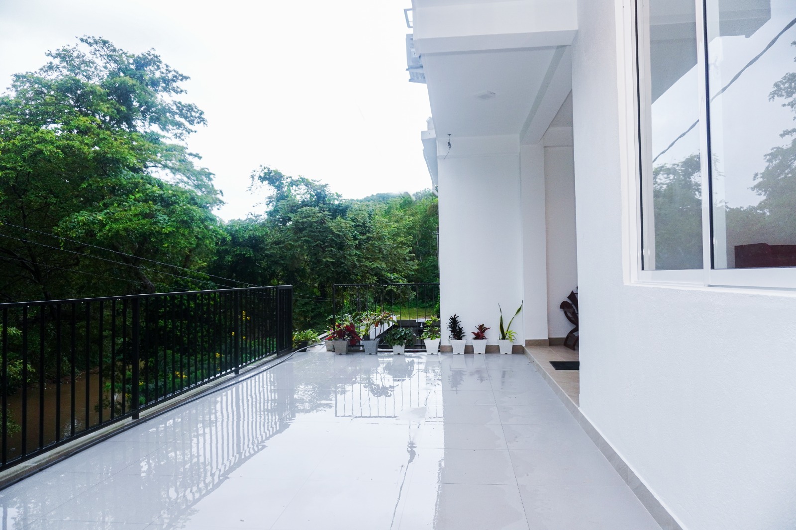 The tiled terrace at Romara Living, with a black railing overlooking tall trees and the river in Oluganthota, Balangoda