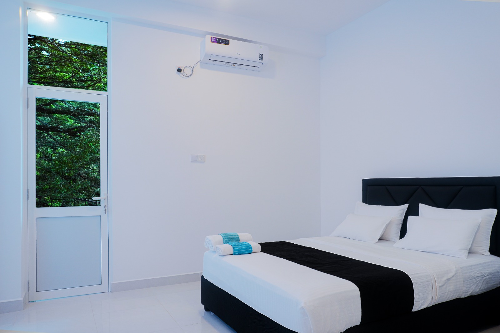 Guest room with a double bed and upholstered headboard, air conditioning and a glass balcony door looking onto green trees